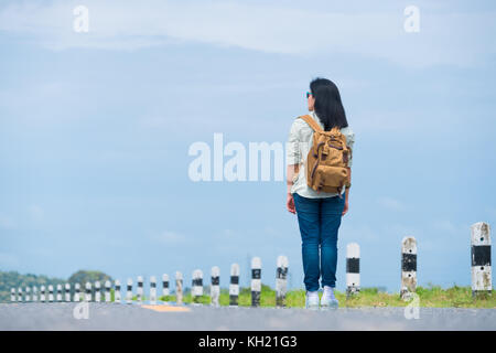 Viaggiatore con zaino guardando il cielo blu,asia donna backpacker permanente sulla strada e guardare avanti per vedere il modo,la libertà viaggio concetto,hitchhiker tr Foto Stock