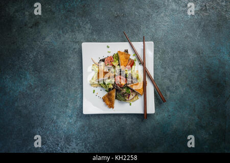 Pan-asiatica, insalata di verdure con pollo fritto. su un quadrato bianco con piastra di bastoncini. vista dall'alto. Foto Stock