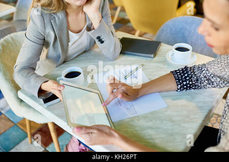 Angolo alto ingrandimento di due giovani donne che lavorano a tavola in cafe con tavoletta digitale durante la riunione di affari Foto Stock