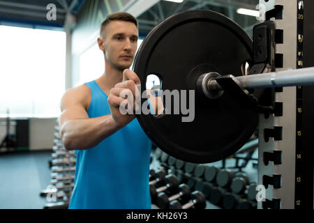 Ritratto di bel giovane impostazione barbell mettendo le piastre pesanti su di esso durante gli allenamenti in palestra moderna Foto Stock