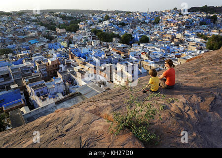 Madre e figlio seduti sulla roccia e guardando la città blu di Jodhpur, Rajasthan, India. Foto Stock