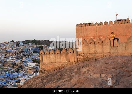 Giovane ragazzo in piedi sulla parete mediante il Forte Mehrangarh e con la vista della città blu di Jodhpur, Rajasthan, India. Foto Stock