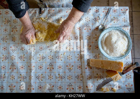 Il vecchio donna fare la pasta fatta in casa con il formaggio parmigiano reggiano Foto Stock