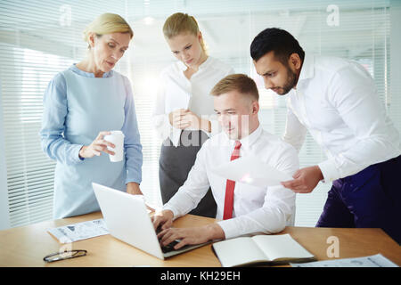 Un gruppo di uomini di affari che guardando la teleconferenza nella parte anteriore del computer portatile in ufficio Foto Stock