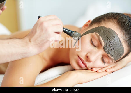 Donna relax nella spa salone mentre cosmetico di applicare la maschera di argilla sul suo viso Foto Stock