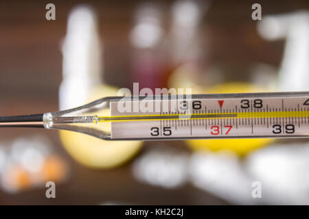 Vetro termometro a mercurio con una elevata temperatura di 37,5 contro lo sfondo di farmaci, limone, tè, rimedi popolari, compresse, spray. diagnosi di Foto Stock