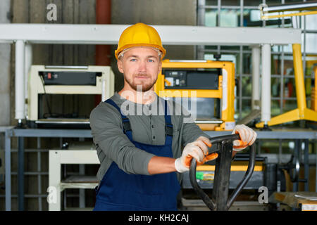 Ritratto di Allegro giovane lavoratore che indossa hardhat che pongono guardando la fotocamera mentre si lavora al moderno stabilimento Foto Stock