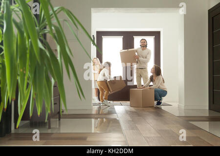 Famiglia felice con bambini che tengono scatole con effetti personali, coppia eccitata e bambini in piedi in un corridoio di casa moderna che guardano intorno si spostano da soli Foto Stock