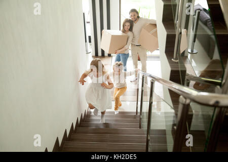 Dei bambini felici di andare al piano di sopra all'interno di due piani di grande casa, eccitati i bambini divertendosi stepping salendo le scale in esecuzione nelle loro camere mentre i genitori tenere premuto Foto Stock