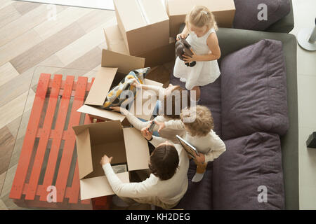 I bambini per aiutare i genitori a disimballare scatole sul divano nel soggiorno accogliente, felice di giovani famiglie con bambini che si divertono in una nuova casa insieme seduta sul lettino, m Foto Stock