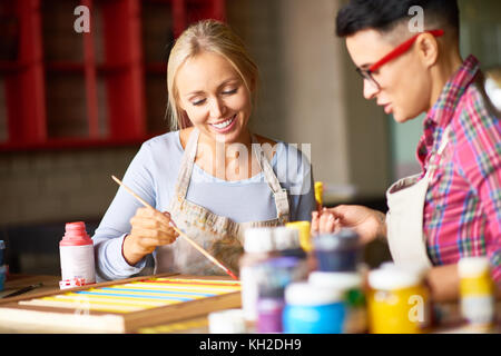 Ritratto di due moderni artisti femmina godendo lavorando insieme in studio d'arte pittura foto, concentrarsi sulla bella bionda donna sorridente felicemente Foto Stock