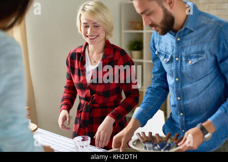 Gruppo di sorridere giovani permanente al grande tavolo con il cibo su di esso la preparazione di vacanza a cena insieme la raccolta a casa Foto Stock