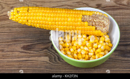 Parzialmente vuoto tutolo di mais e heap di mais bollito. giallo grani di mais in vaschetta rotonda e parzialmente rosicchiati cob su uno sfondo di legno. Foto Stock