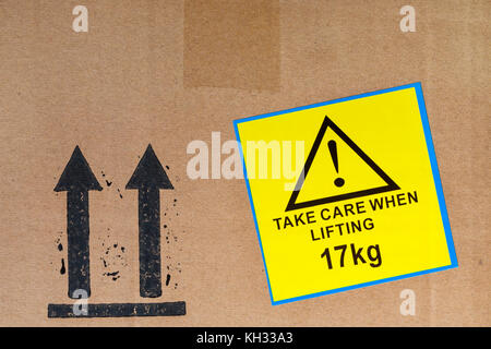 Prestare attenzione durante il sollevamento di 17kg di adesivo giallo etichetta incollata su una scatola di cartone e mantenere il montante Frecce simbolo Foto Stock