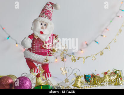 Babbo natale decorazione giocattolo imbottito, su sfondo bianco e la superficie, con colorati bokeh luci e decorazioni natalizie in background Foto Stock