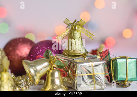 Decorazione di natale, regali, catene, campane e colorato sfere riflettenti, sulla sommità di un bianco superficie di legno e sfondo bianco, con sfondo bokeh di fondo Foto Stock