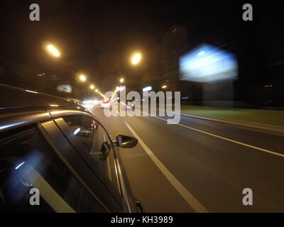La vettura è in movimento ad alta velocità su strada di notte nella città. Lato della telecamera sul corpo vettura. Foto Stock