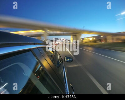 La vettura è in movimento ad alta velocità su strada di notte nella città. Lato della telecamera sul corpo vettura. Foto Stock