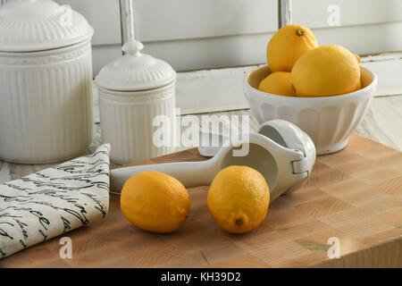 Freschi limoni organico-bianco e giallo con gli agrumi hand-held spremiagrumi, leggero e luminoso su un tagliere di legno Foto Stock