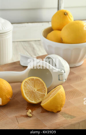 Freschi limoni organico-bianco e giallo con gli agrumi hand-held spremiagrumi, leggero e luminoso su un tagliere di legno-posizionamento verticale Foto Stock