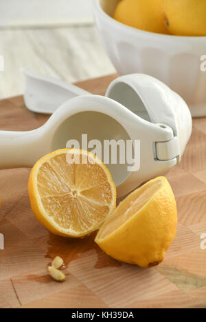 Freschi limoni organico-bianco e giallo con gli agrumi hand-held spremiagrumi, leggero e luminoso su un tagliere di legno-orientamento verticale Foto Stock