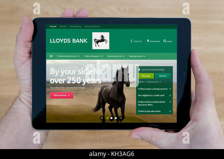 Un uomo guarda alla Banca di Lloyds sito sul suo iPad dispositivo tablet, sparato contro un tavolo di legno top sfondo (solo uso editoriale) Foto Stock