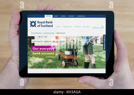 Un uomo guarda la banca RBS sito sul suo iPad dispositivo tablet, sparato contro un tavolo di legno top sfondo (solo uso editoriale) Foto Stock
