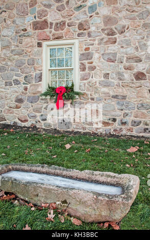 Vecchia casa di pietra, ghirlanda di Natale swag sulla finestra, vecchio trogolo di acqua per cavalli, Lancaster County, Pennsylvan, Usa, agricoltura verticale, noi inverno vintage Foto Stock