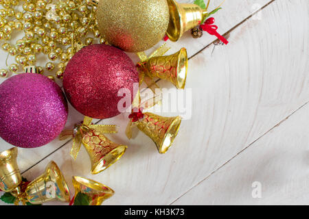 Decorazione di natale, catene, campane e colorato sfere riflettenti, sulla sommità di un bianco superficie di legno e sfondo bianco Foto Stock