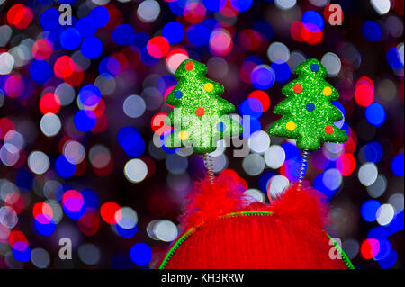 Molleggiante decorativo di alberi di Natale sulle novità headwear in piedi contro colorato bokeh bolle di luce Foto Stock