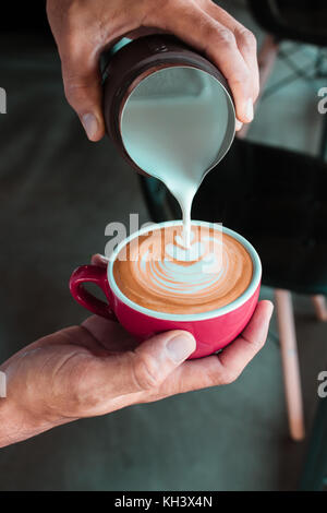 Versare il latte dal lanciatore fare il caffè latte art da barista in coffee shop Foto Stock