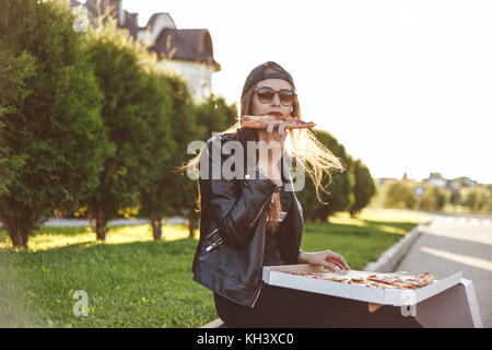 Allegro giovane donna godendo di un trancio di pizza seduti sul cordolo outdoor Foto Stock