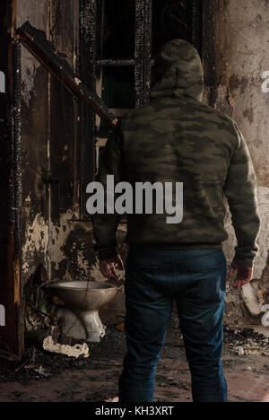 Uomo che indossa il camuffamento cofano in casa bruciata Foto Stock