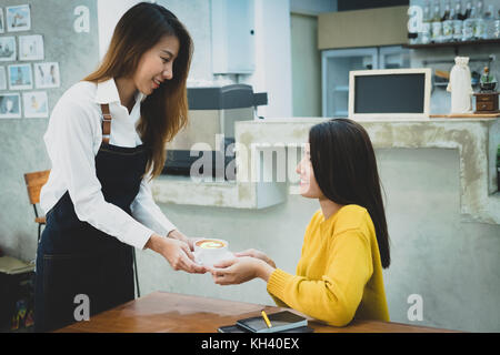 Sorridente asian barista serve una tazza di caffè al cliente. cafe restaurant service, industria alimentare e delle bevande del concetto. Foto Stock