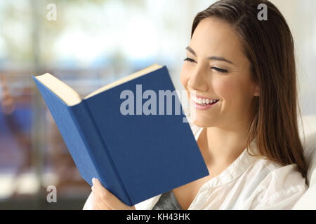 Lettore di felice leggendo un libro seduto su un divano nel soggiorno di casa Foto Stock