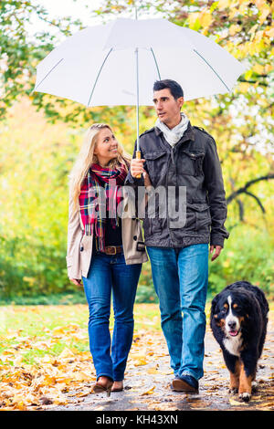 Donna e uomo avente la passeggiata con il cane in autunno la pioggia Foto Stock