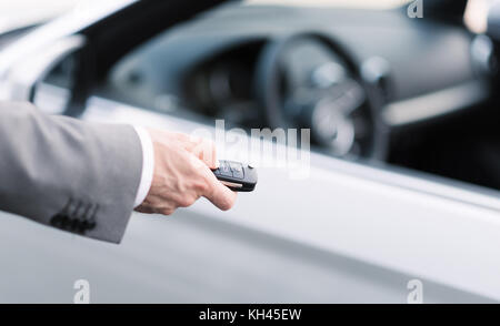 Imprenditore tenendo premuto un tasto auto con telecomando e premendo un pulsante, egli è di sbloccare la porta, canto close up Foto Stock