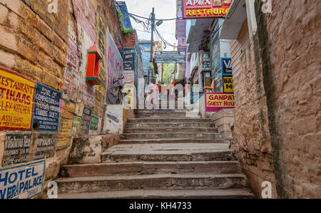 Vecchia città di Varanasi vicoletto con case vintage pareti in mattoni e ripide e strette scalinate. Una vecchia donna visto scendendo le scale. Foto Stock