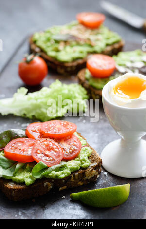 Avocado toast con spinaci, pomodoro e uova sode. Verde sano veggie sandwich aperto. Messa a fuoco selettiva Foto Stock