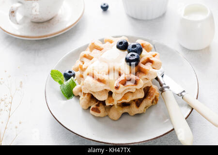 Cialde belghe con crema di miele e mirtilli sulla piastra bianca. Prima colazione luminosa immagine Foto Stock
