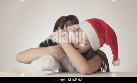 Bella ragazza adolescente in santa claus hat felicemente abbraccia il suo cane su sfondo bianco Foto Stock