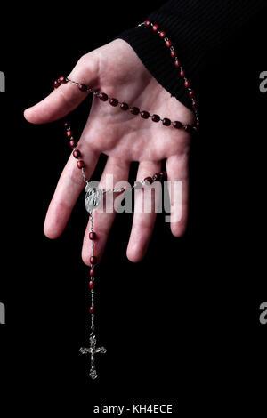 Mani femminili holding e appendere un rosario con Gesù Cristo in croce o crocifisso su sfondo nero. donna con cristiana cattolica fede religiosa Foto Stock