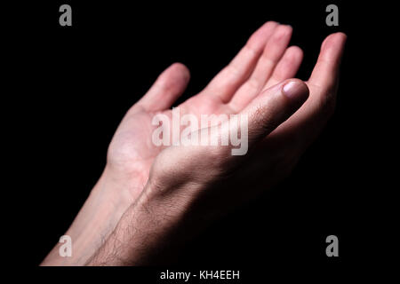 Maschio pregando le mani con i palmi rivolti verso l'alto braccia tese. sfondo nero. close up man mano. concetto per la preghiera, la fede, la religione, religiosi, di culto Foto Stock