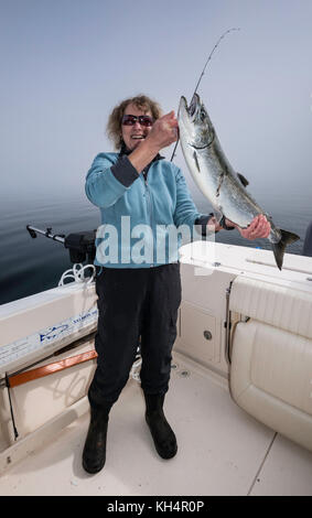 Donna di mezza età in barca da pesca con catturato il salmone, mattinata nebbiosa a Johnstone Strait fuori dall'Isola di Vancouver, British Columbia, Canada Foto Stock