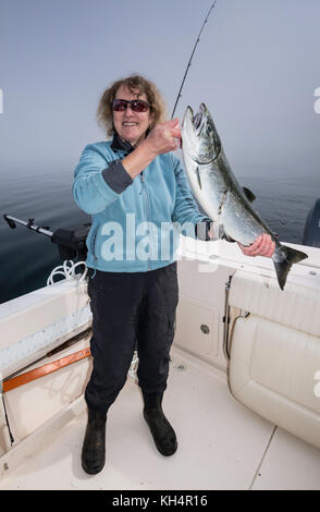 Donna di mezza età in barca da pesca con catturato il salmone, mattinata nebbiosa a Johnstone Strait fuori dall'Isola di Vancouver, British Columbia, Canada Foto Stock