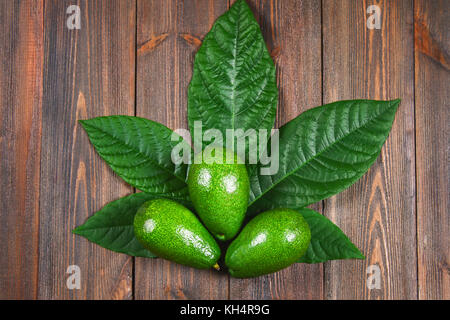 Tre materie verde avocado maturo con foglie giacciono sotto forma di canapa su una tavola di legno marrone a tavola. Foto Stock