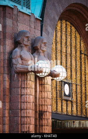 Helsinki, Finlandia. vista notturna di due coppie di statue tenendo le lampade sferiche su ingresso a Helsinki la stazione ferroviaria centrale. La sera o la notte il Foto Stock