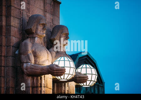 Helsinki, Finlandia. vista notturna di due coppie di statue tenendo le lampade sferiche su ingresso a Helsinki la stazione ferroviaria centrale. La sera o la notte il Foto Stock