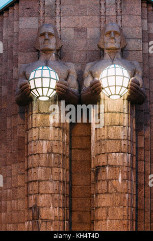 Helsinki, Finlandia. vista notturna di due coppie di statue tenendo le lampade sferiche su ingresso a Helsinki la stazione ferroviaria centrale. La sera o la notte il Foto Stock