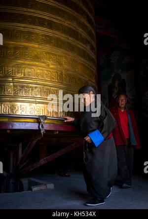 Pellegrini tibetani girando enorme ruota di preghiera nel monastero di Rongwo, Tongren County, Longwu, Cina Foto Stock